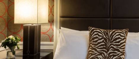 A neatly made bed with white linens and a zebra-patterned pillow, a bedside table with a lamp, and a wall with a geometric pattern.