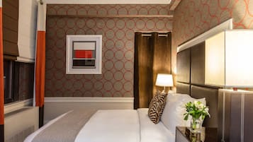 Une chambre d’hôtel avec un lit, une table de chevet avec une lampe, un vase de fleurs et un papier peint à motifs.