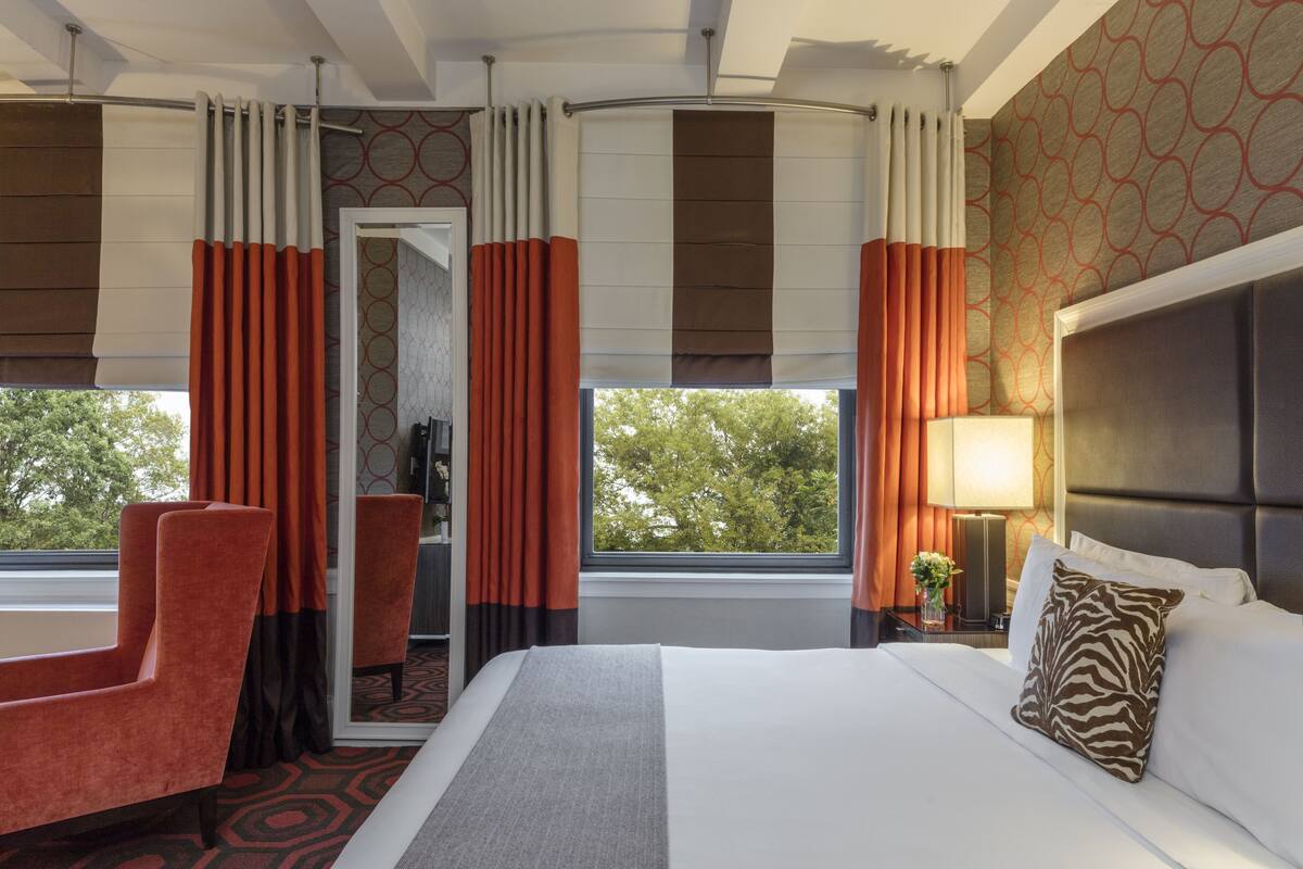 A hotel room with a bed, a chair, a nightstand, and a window with curtains.