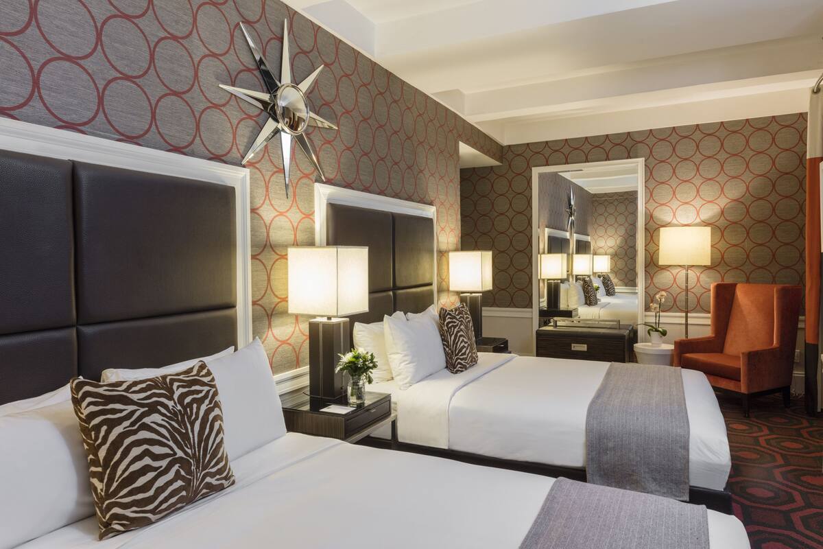 A hotel room with two beds, a large mirror, a star-shaped wall decoration, and a patterned carpet.