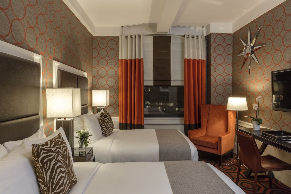 A hotel room with two beds, a desk, a chair, a TV, and a window with curtains.