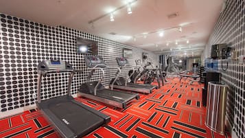 Ein Fitnessraum mit Laufbändern, Crosstrainern und einem roten, gemusterten Boden.