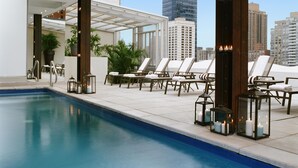 A rooftop pool area with lounge chairs, candles, and a view of city buildings.