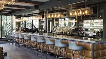 Una zona de bar moderna con una barra larga, varios taburetes y una gran variedad de botellas y vasos.