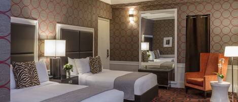A hotel room with two beds, a sitting area with a chair, a small table, and a mirror.