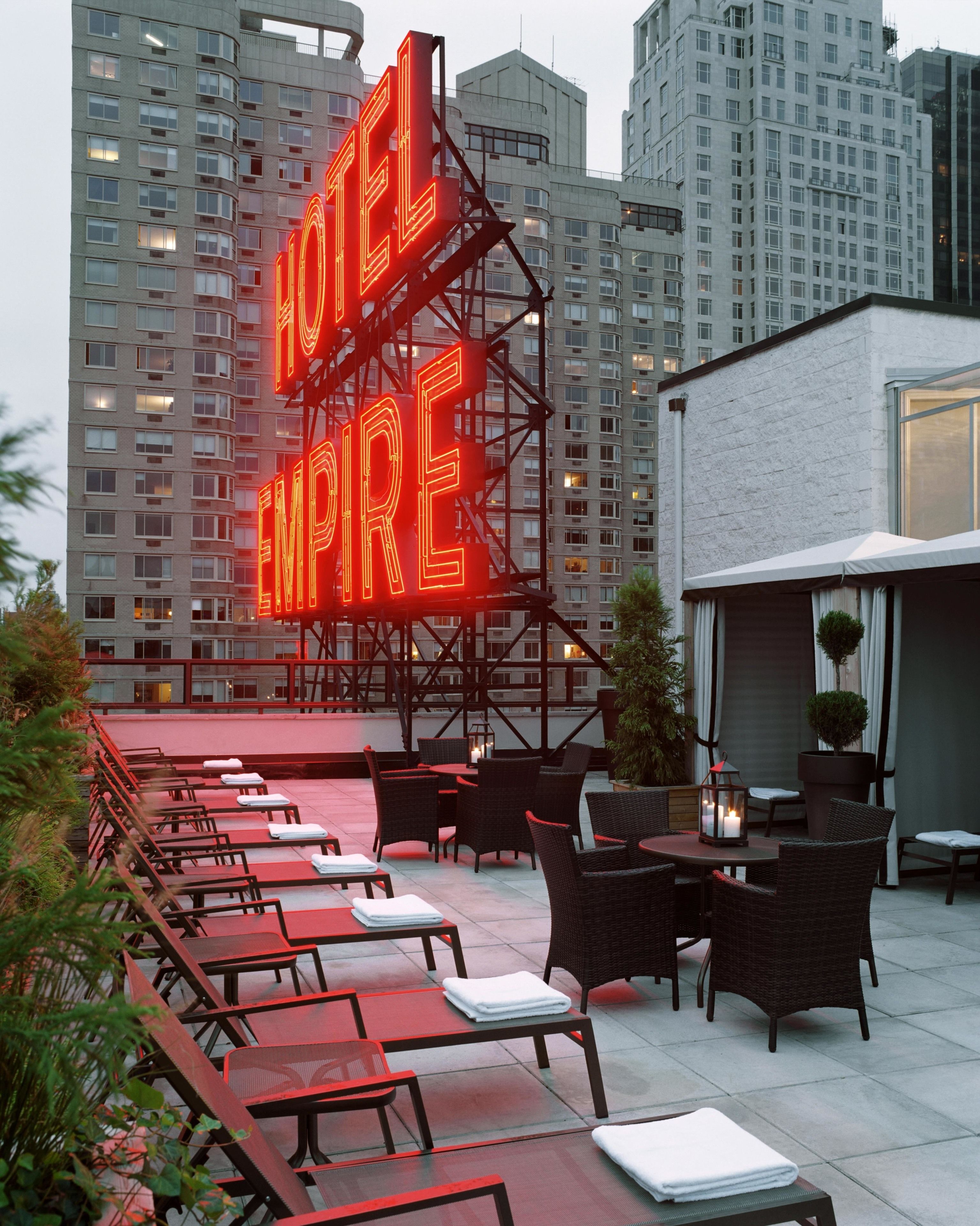 Una terraza en la azotea con mobiliario exterior y un letrero de neón que dice "HOTEL EMPIRE".