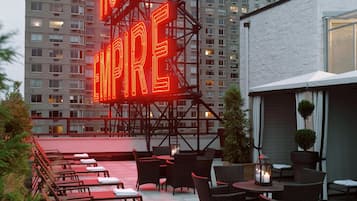 Una terraza en la azotea con mobiliario exterior y un letrero de neón que dice "HOTEL EMPIRE".
