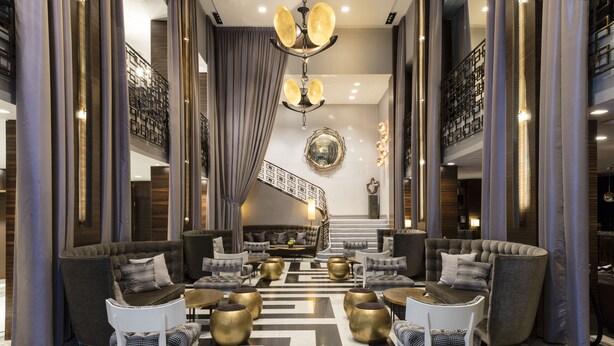 A spacious lobby with a central staircase, modern seating arrangements, and a chandelier.