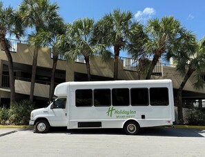 A white bus with 'Holiday Inn Miami West' branding parked in front of a building with palm trees. - Holiday Inn Miami West - Airport Area by IHG (Hialeah)