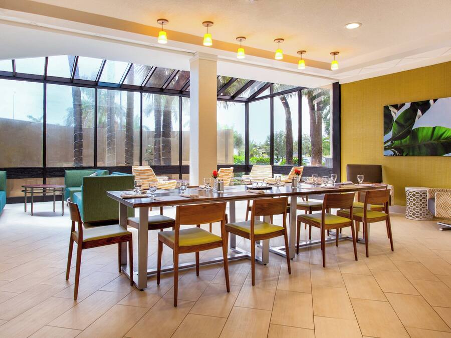 A spacious dining area with a large table, multiple chairs, and a view of palm trees through large windows.