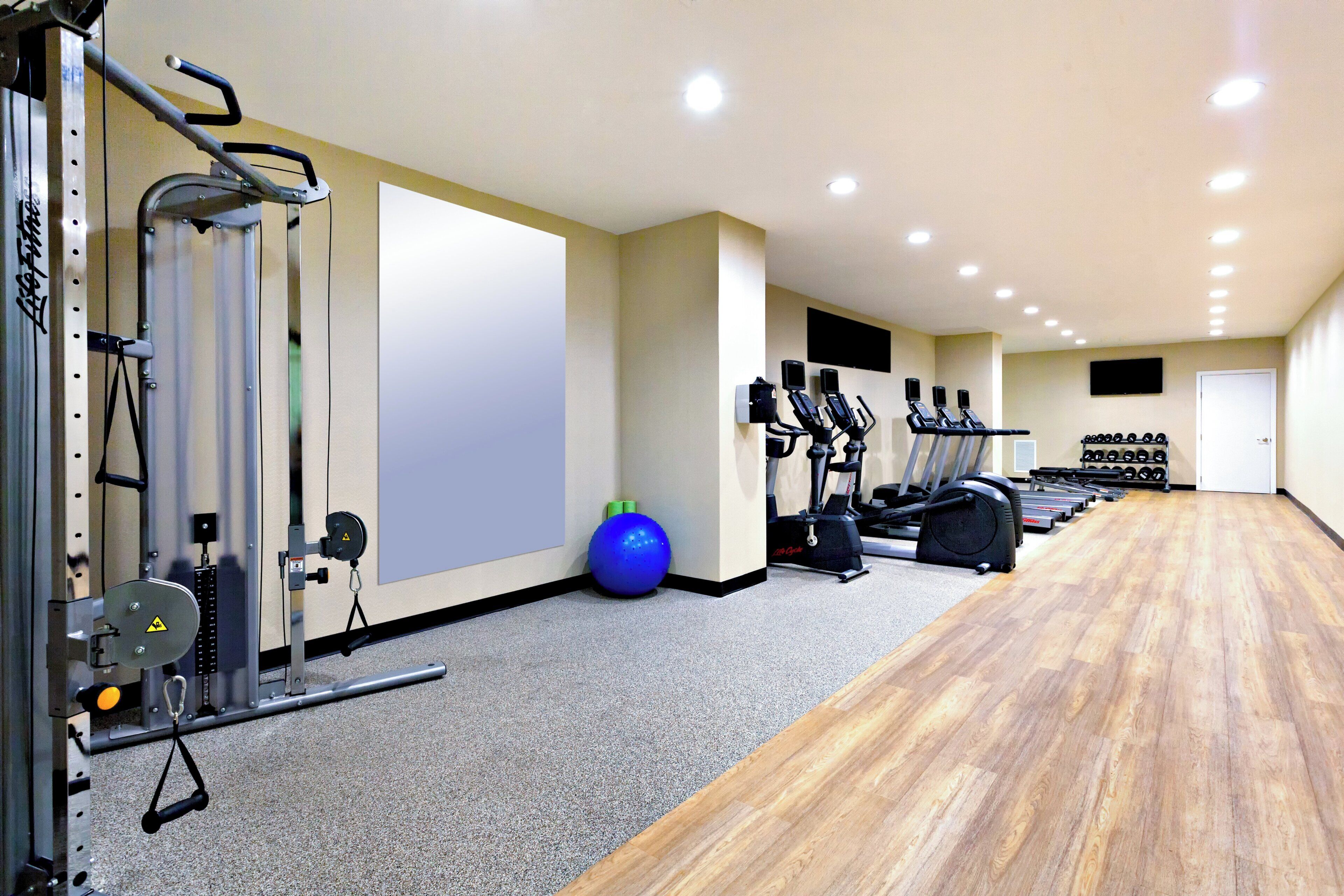 Un gimnasio con máquinas de cardio, equipo de levantamiento de pesas y una pelota de ejercicio azul.