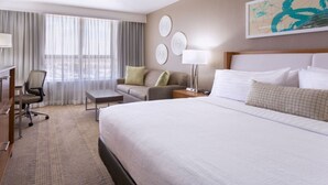 A hotel room with a large bed, a desk, a chair, a sofa, and a window with curtains. - Holiday Inn Miami West - Airport Area by IHG (Hialeah)