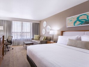 A hotel room with a large bed, a desk, a chair, a sofa, and a window with curtains.