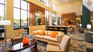 A hotel lobby with a sofa, armchairs, a coffee table, and a dining area with chairs and a table. - Holiday Inn Miami West - Airport Area by IHG (Hialeah)