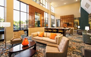 A hotel lobby with a sofa, armchairs, a coffee table, and a dining area with chairs and a table. - Holiday Inn Miami West - Airport Area by IHG (Hialeah)