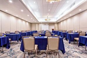 Une salle de conférence avec des rangées de tables, des chaises et un écran de projection.