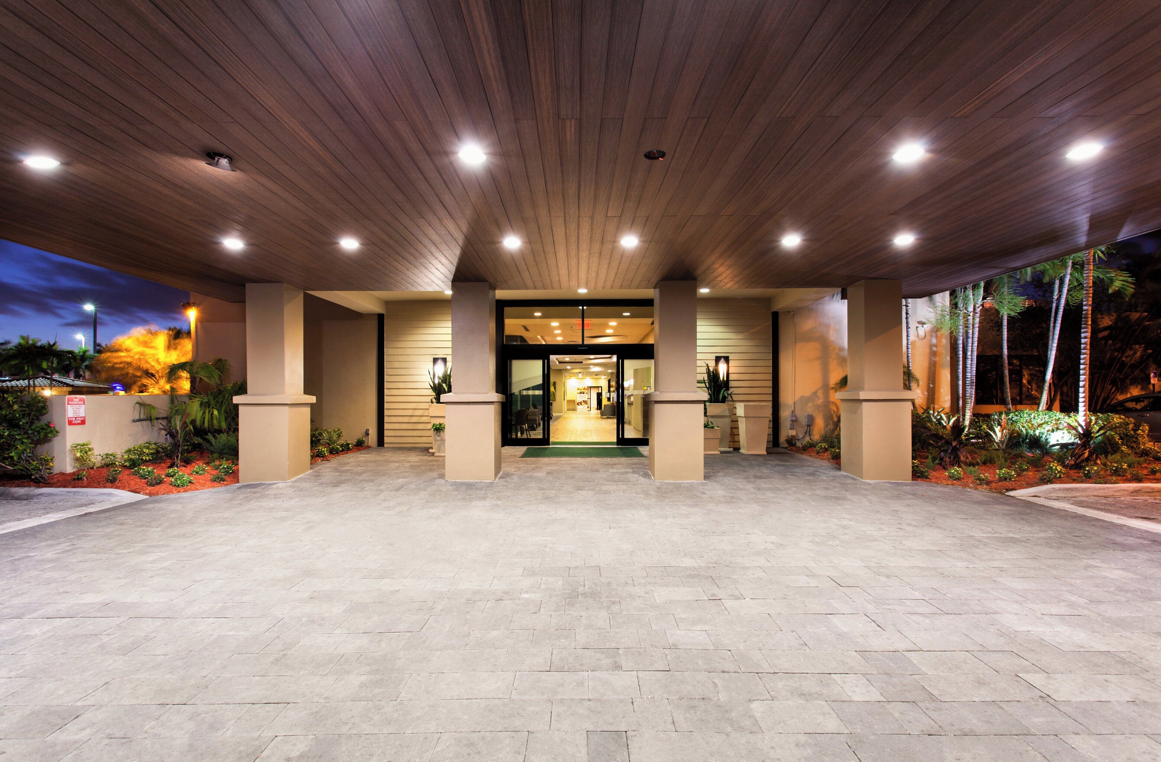 A hotel entrance with a covered walkway, columns, and a well-lit interior visible through the doors.