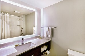 A bathroom with a large mirror, a sink, a toilet, and a shower area.