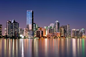 A city skyline at dusk with high-rise buildings reflecting on a calm body of water.