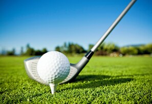 A golf ball on a tee on a green with a golf club in the background. - Holiday Inn Miami West - Airport Area by IHG (Hialeah)