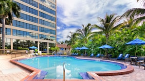 A swimming pool with blue umbrellas, lounge chairs, and palm trees. - Holiday Inn Miami West - Airport Area by IHG (Hialeah)