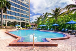 A swimming pool with blue umbrellas, lounge chairs, and palm trees.