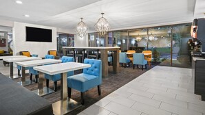 A modern dining area with white tables and blue chairs, large windows, and decorative chandeliers. - La Quinta Inn & Suites by Wyndham Sturbridge (Fiskdale)