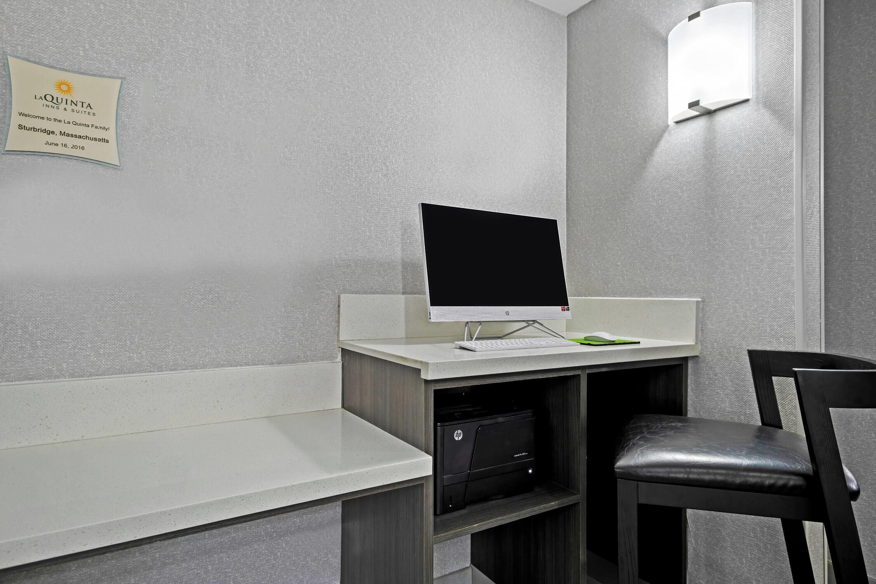 Een hotelkamer met een bureau, een computer, een stoel en een kleine prullenbak.