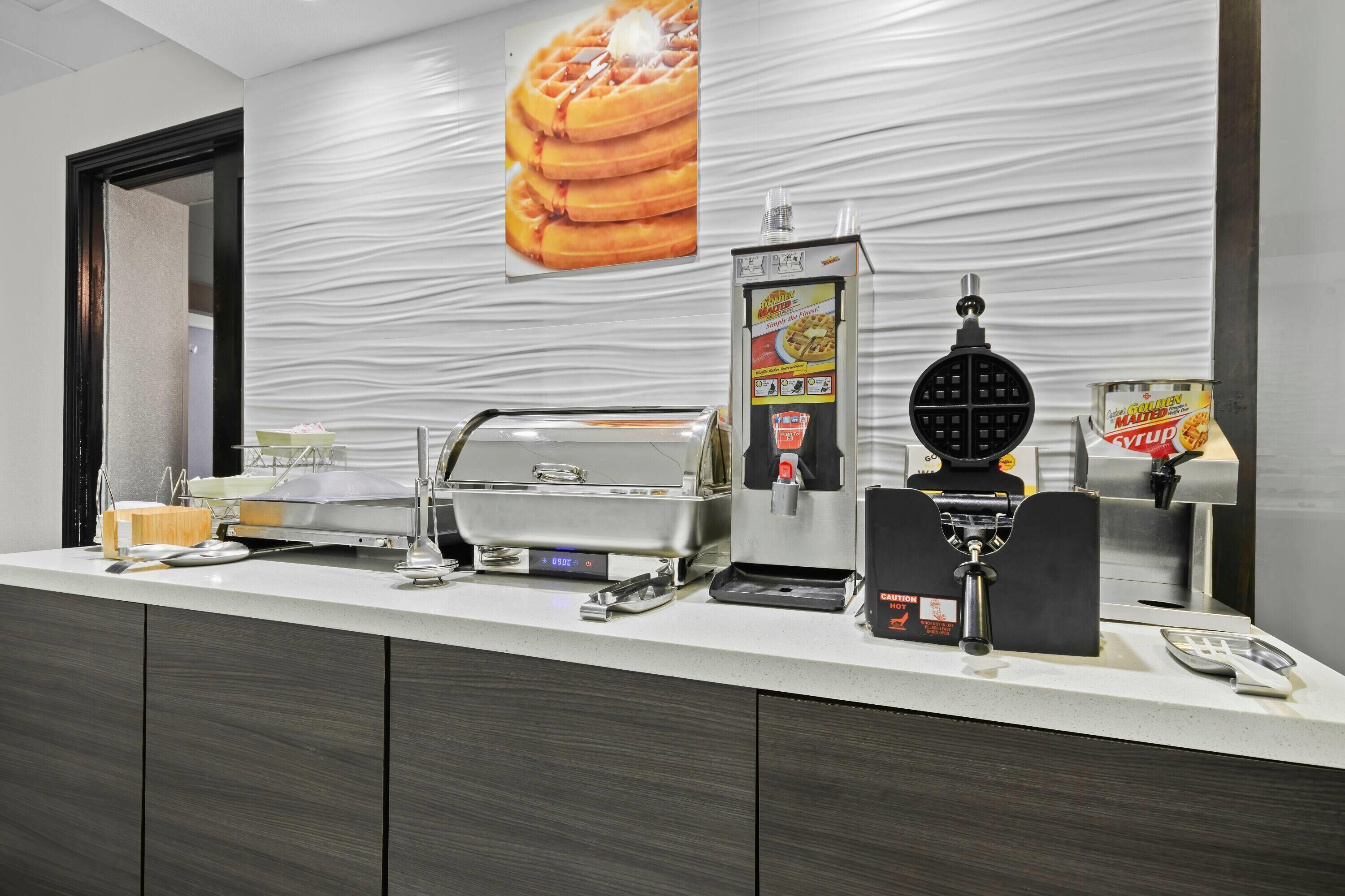 A breakfast bar with waffle makers, syrup dispensers, and a coffee machine.