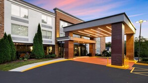 A modern hotel entrance with a covered walkway, large windows, and a landscaped area. - La Quinta Inn & Suites by Wyndham Sturbridge (Fiskdale)