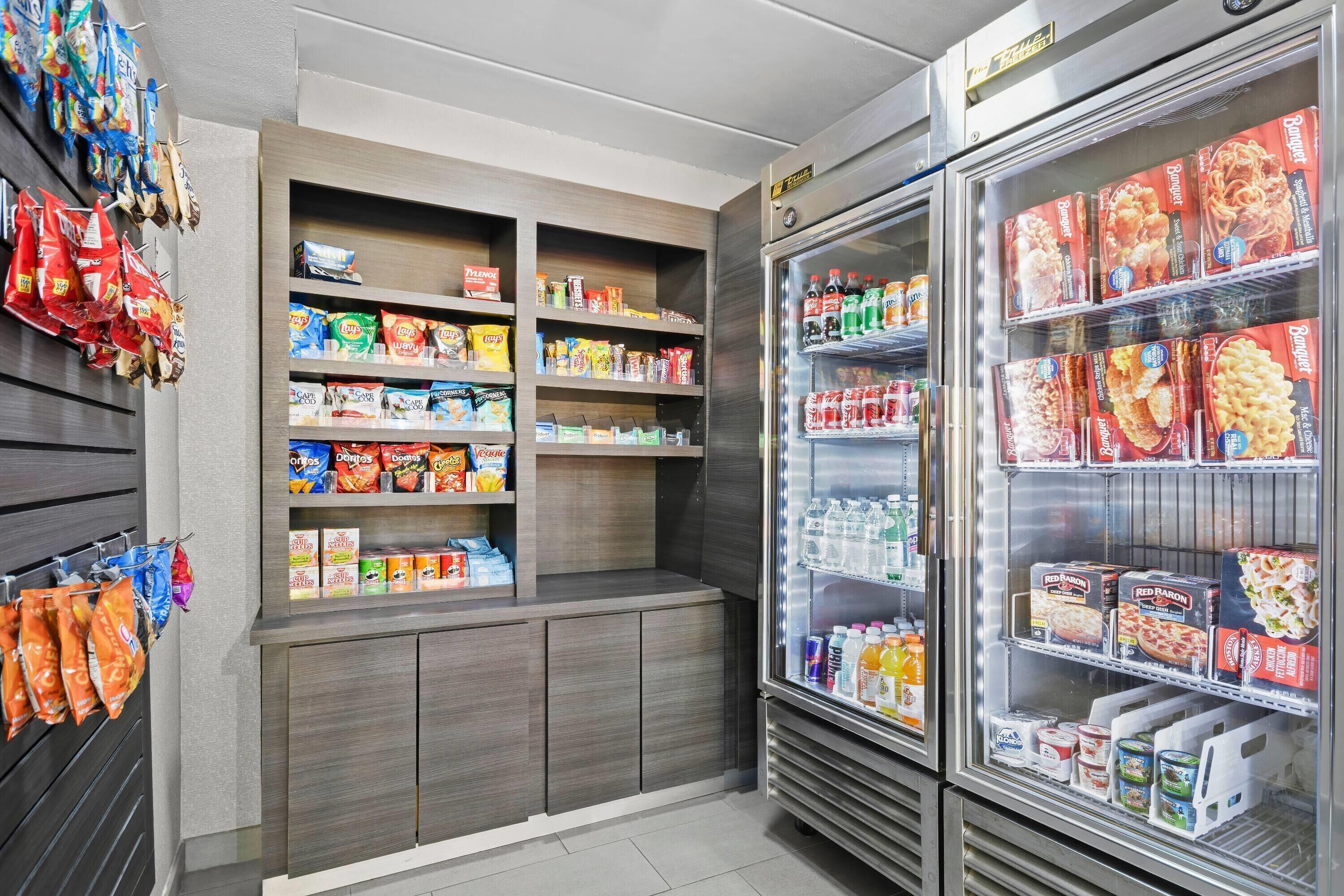 Una sección de aperitivos y bebidas con estantes llenos de diversas opciones, y un expositor refrigerado con alimentos congelados.