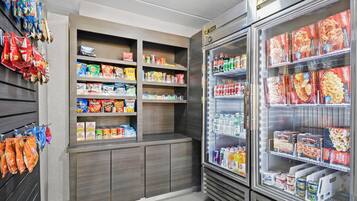 Una sección de aperitivos y bebidas con estantes llenos de diversas opciones, y un expositor refrigerado con alimentos congelados.