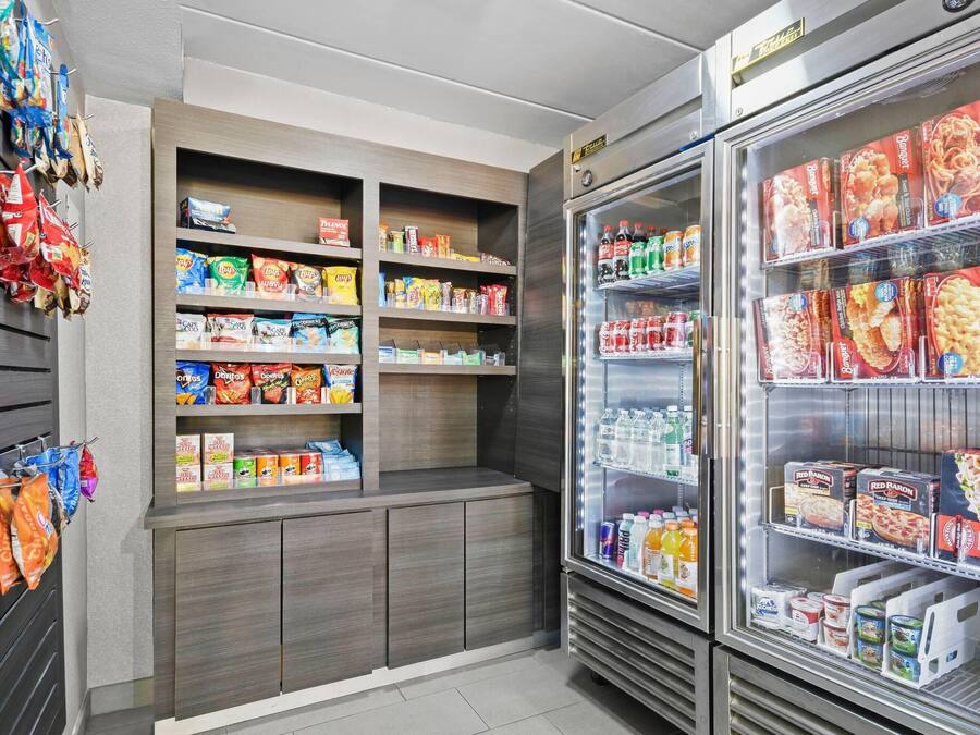 Una sección de aperitivos y bebidas con estantes llenos de diversas opciones, y un expositor refrigerado con alimentos congelados.
