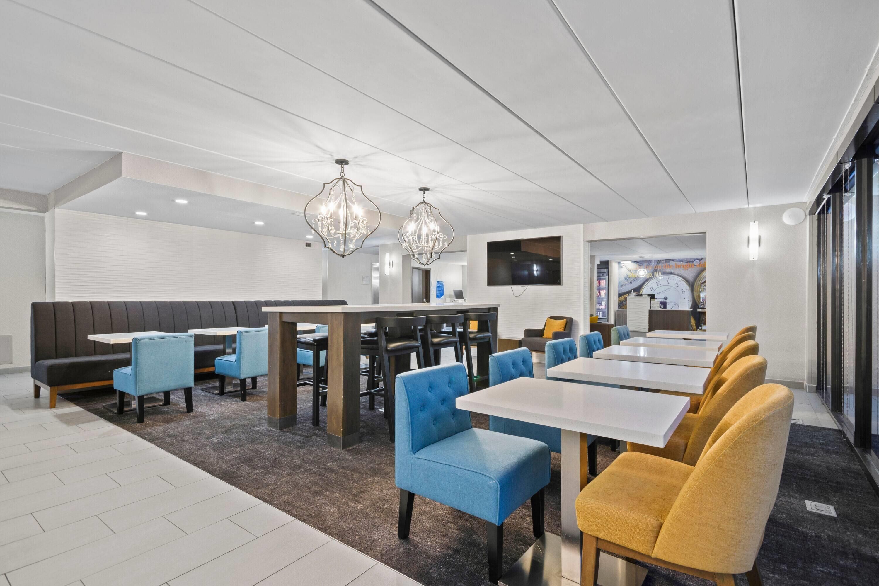 A modern dining area with a mix of blue and yellow chairs, a central table, and decorative crystal chandeliers.