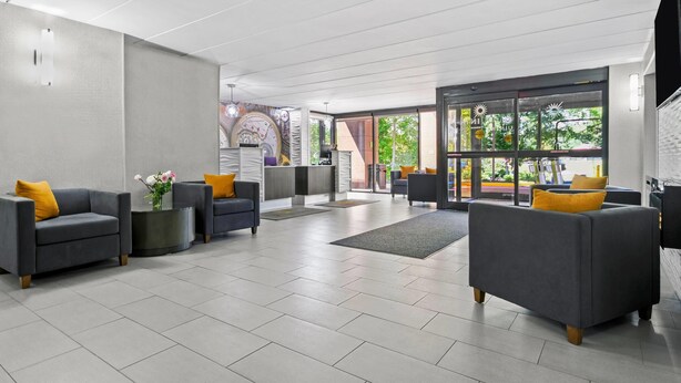 A modern lobby with grey sofas, a reception desk, and large windows offering views of greenery. - La Quinta Inn & Suites by Wyndham Sturbridge (Fiskdale)