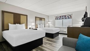 A hotel room with two beds, a desk, a chair, and a large window with a geometric curtain. - La Quinta Inn & Suites by Wyndham Sturbridge (Fiskdale)