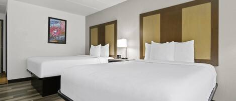 Una habitación de hotel con dos camas, una mesita de noche, una lámpara y un cuadro en la pared.