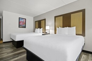 Una habitación de hotel con dos camas, una mesita de noche, una lámpara y un cuadro en la pared.