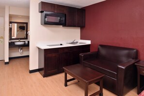 A compact kitchenette with a microwave, sink, and cabinet, a small wooden table, and a leather chair.