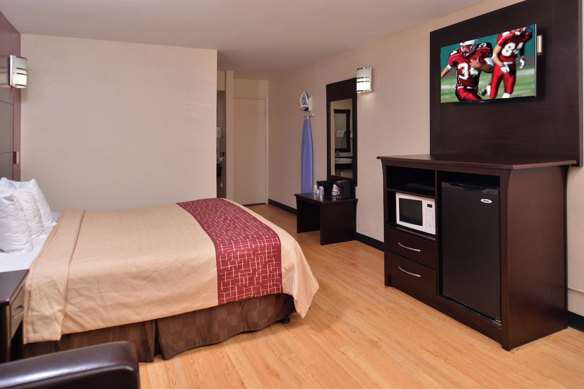 A hotel room with a bed, a TV mounted on the wall, a microwave, and a small table with a mirror.