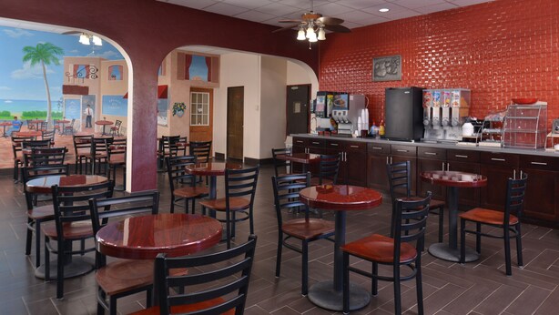 A restaurant with multiple tables and chairs, a bar area, and a mural of a beach scene.