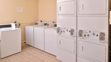 Uma lavanderia com máquinas de lavar e secar empilhadas, painéis de controle e uma máquina industrial.