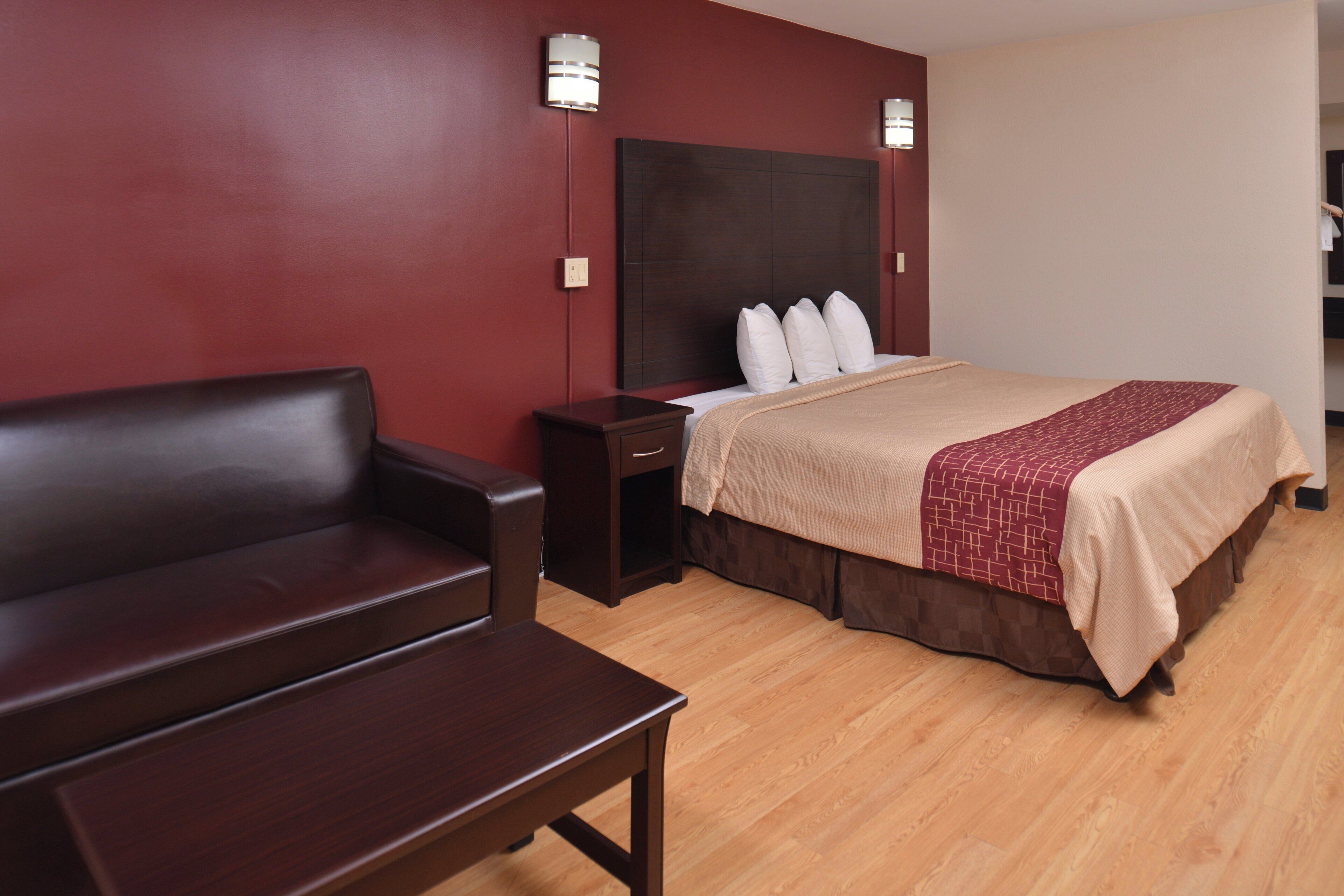 A hotel room with a bed, a sofa, a nightstand, and a wall-mounted lamp.