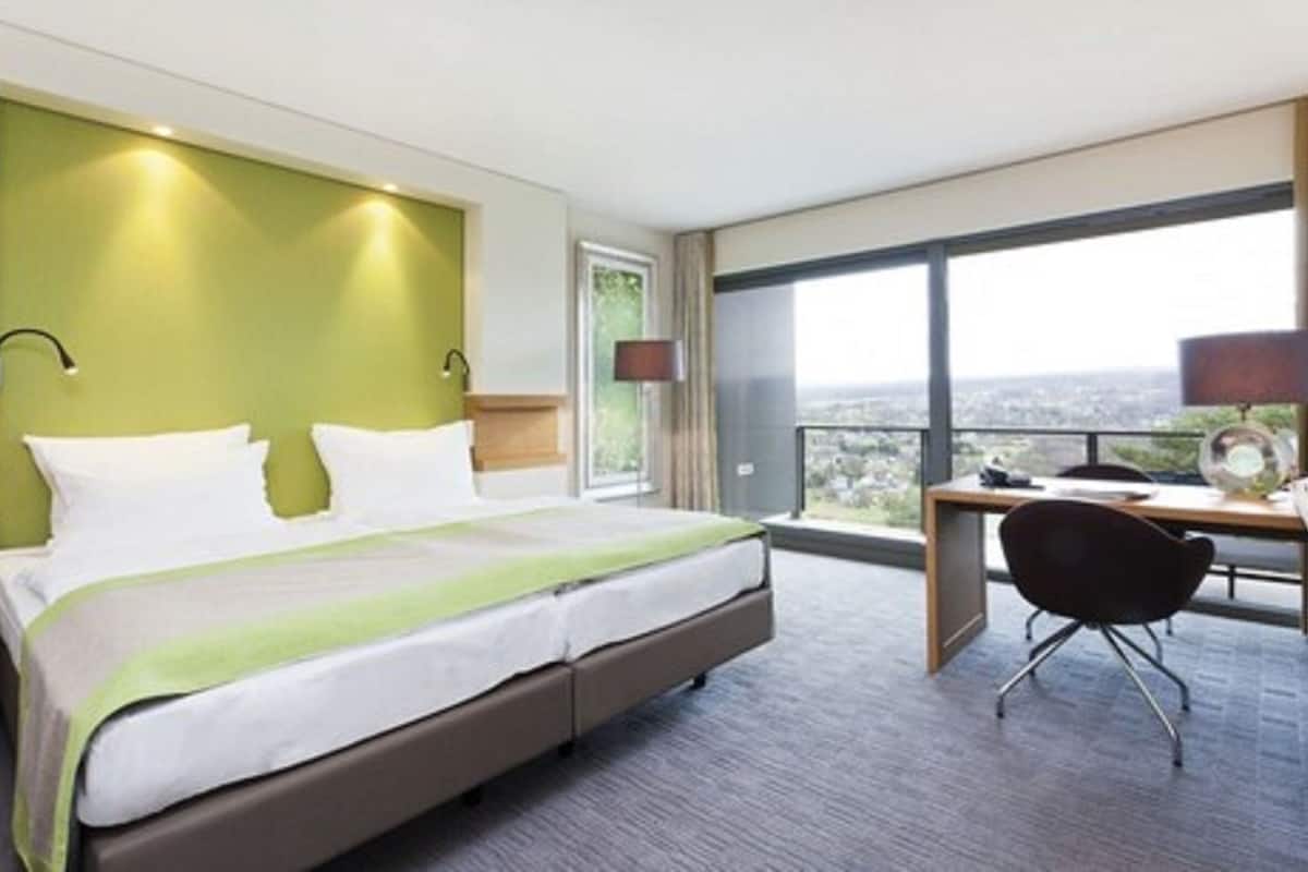 A hotel room with a large bed, a desk, and a view of the city.