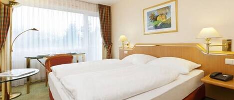 A hotel room with a large bed, a desk, a chair, a lamp, a painting, and a telephone on the nightstand.