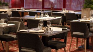 Un restaurante con mesas dispuestas para comer, que presenta una alfombra estampada y cortinas rojas.