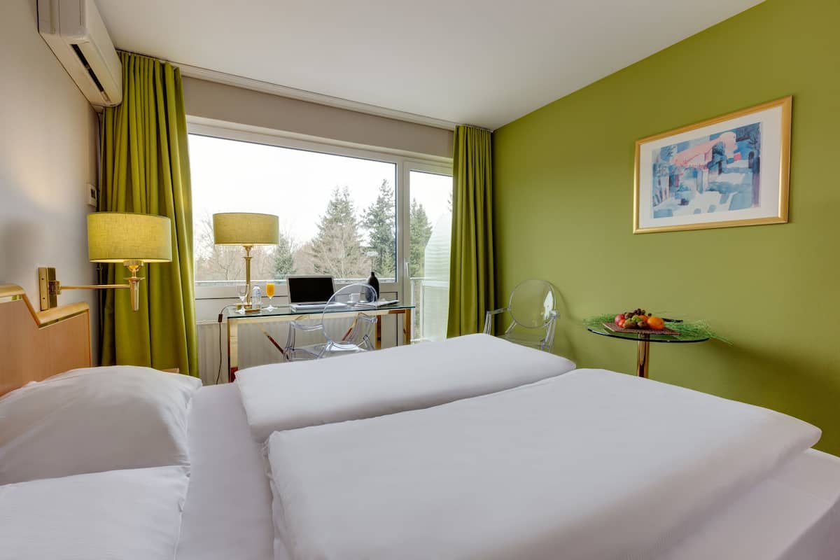 A hotel room with two beds, a desk with a laptop, a small table with fruit, and a painting on the wall.