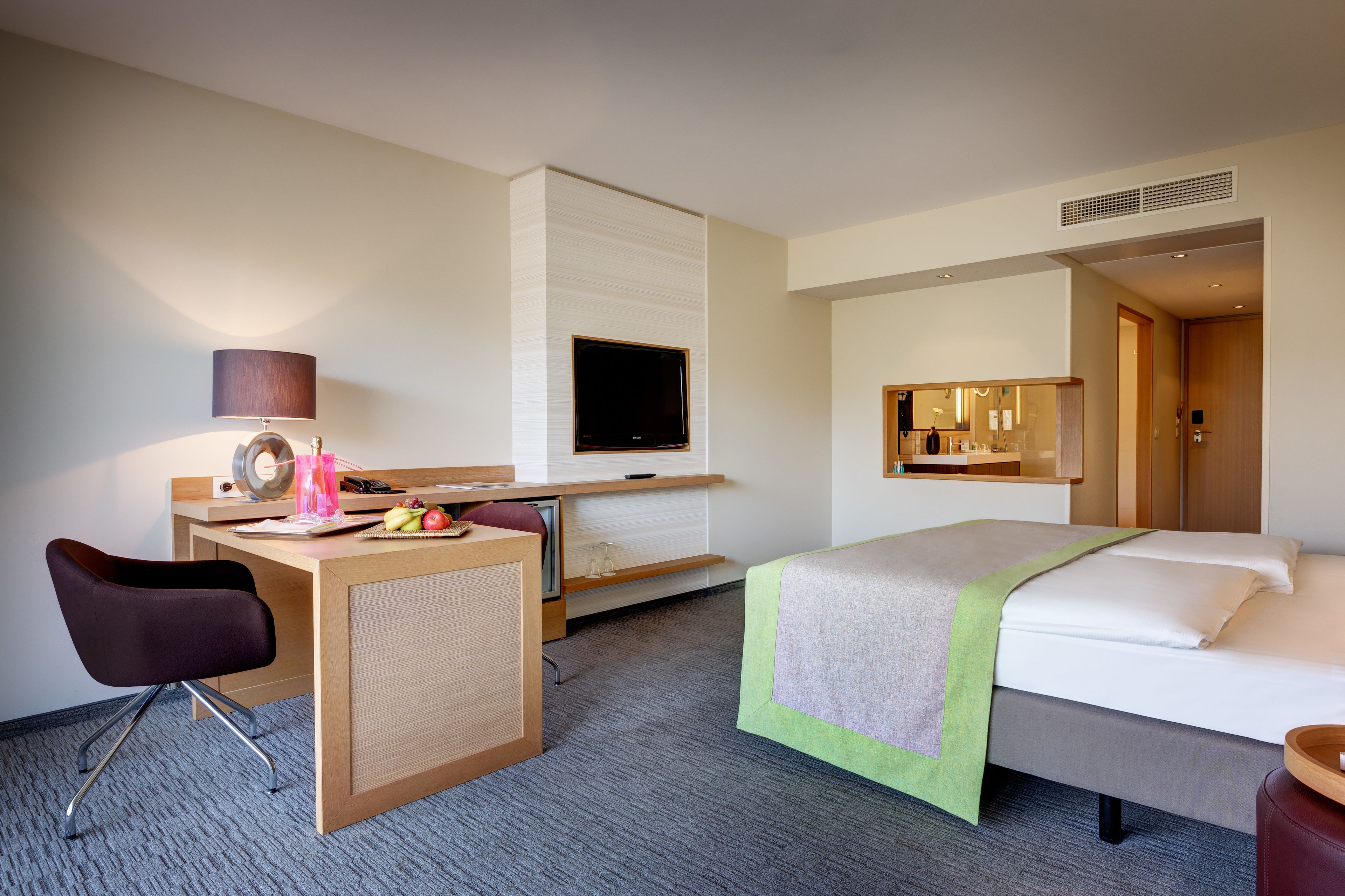 Habitación de hotel con cama, escritorio, silla, televisor y espejo.