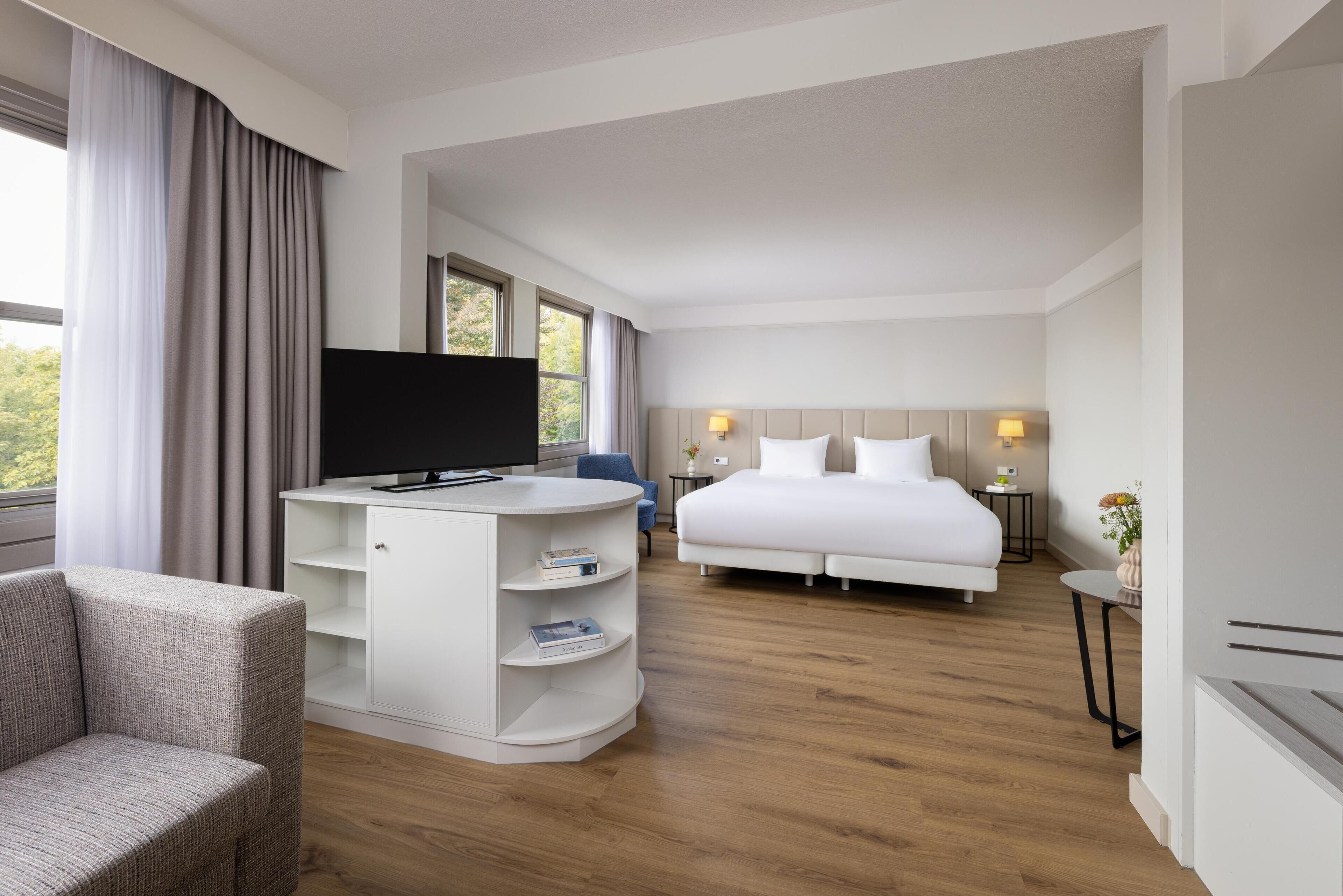 Hotelkamer met een bed, een televisie, een bureau, een stoel en een tafeltje met een lamp.