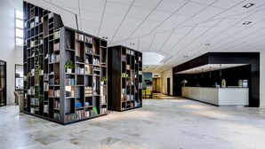 A spacious lobby with a modern design, featuring a large central area with a reception desk, surrounded by tall bookshelves filled with books and plants. - NH Bussum Jan Tabak (Bussum)